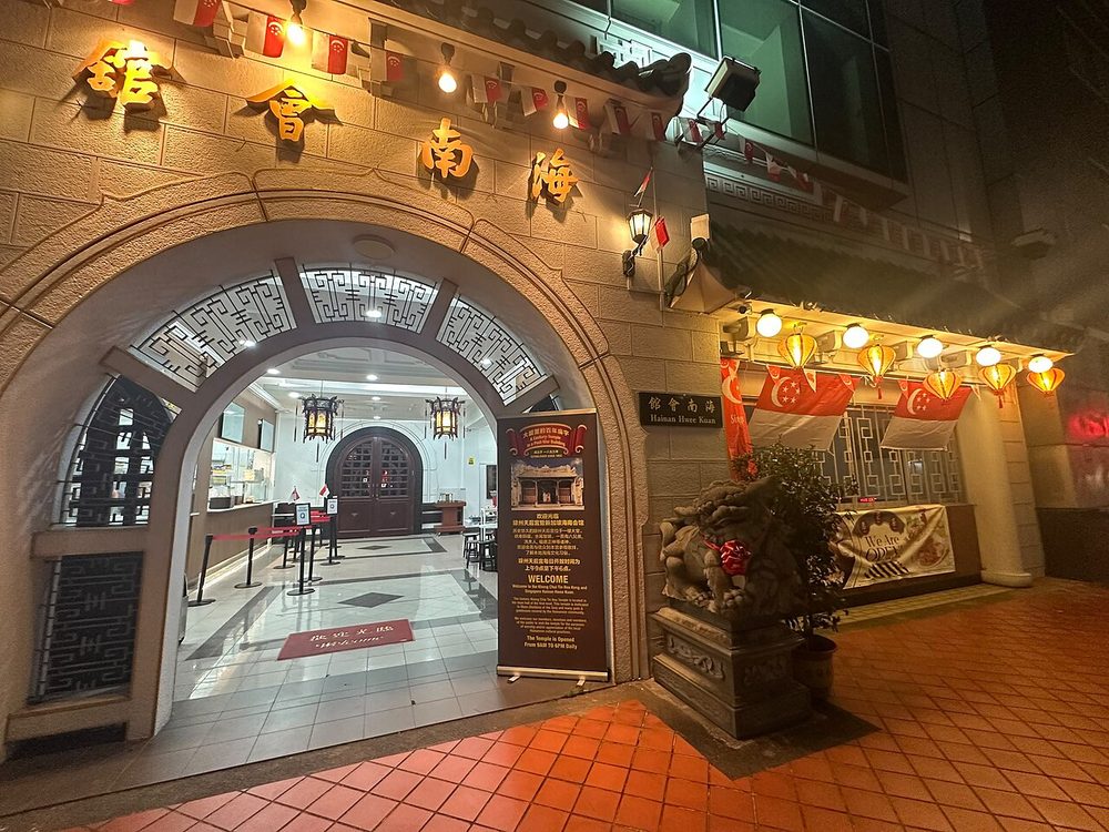 The arched, ornately framed entrance of the Singapore Hainan Hwee Kuan at night, with Chinese characters above the door