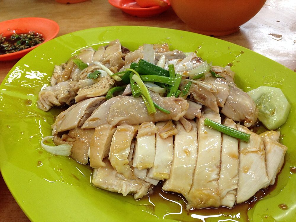 Sliced pale poached chicken with spring onions in a pool of soy and oil on a green plate