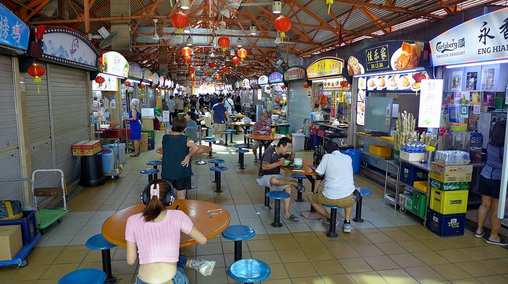 Interior of Maxwell Food Centre, Singapore, with rows of hawker stalls, red lanterns and diners at tables