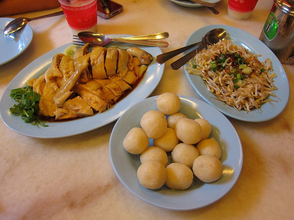 A plate of soy-dressed poached chicken, a bowl of round white rice balls and a plate of bean sprouts, in Melaka