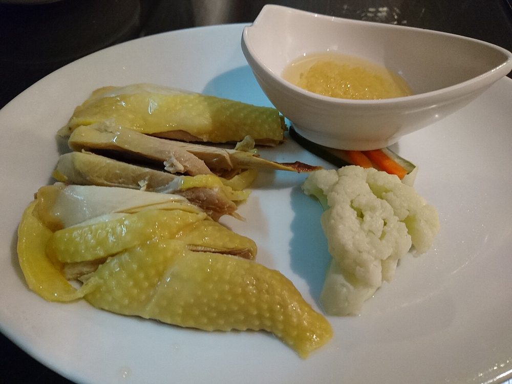 Yellow-skinned poached chicken on a white plate with a dish of pounded ginger sauce