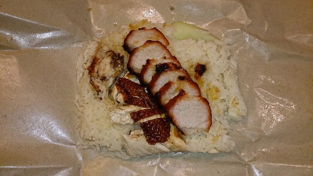 Takeaway rice on waxed paper topped with sliced roast chicken and char siu roast pork