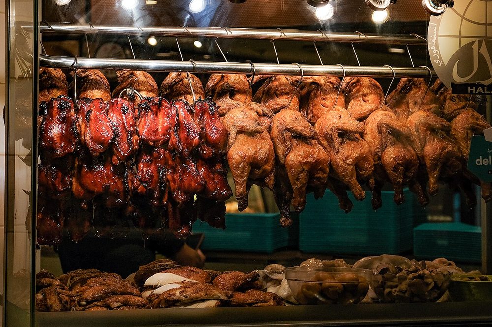 Rows of roast chickens and ducks hanging in the glass window of a chicken rice stall in Singapore