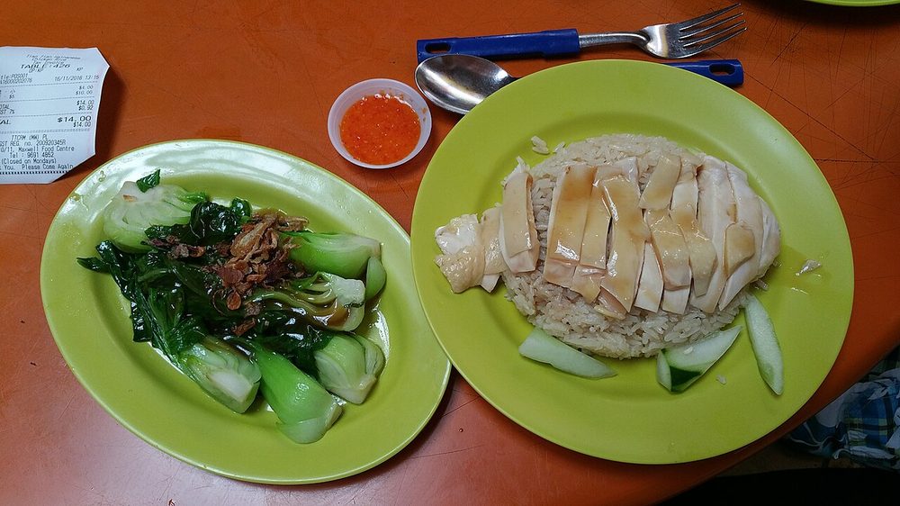 A Tian Tian chicken rice plate with sliced white chicken, a separate plate of greens and a dish of chilli sauce