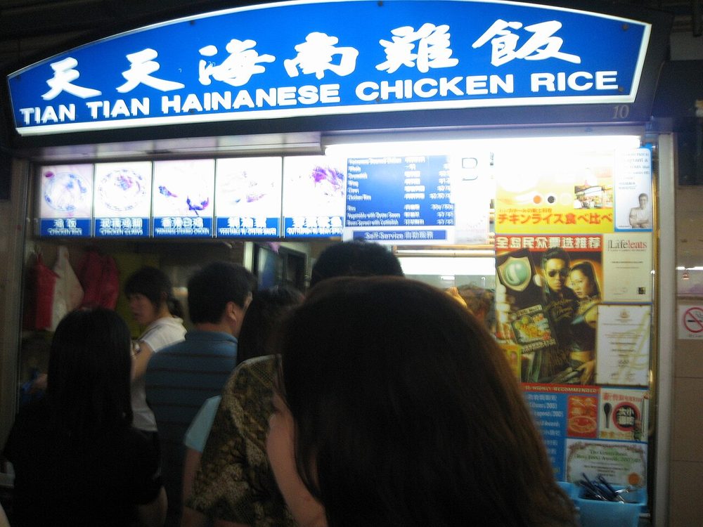 The illuminated signboard of Tian Tian Hainanese Chicken Rice at Maxwell Food Centre with a queue of customers in front