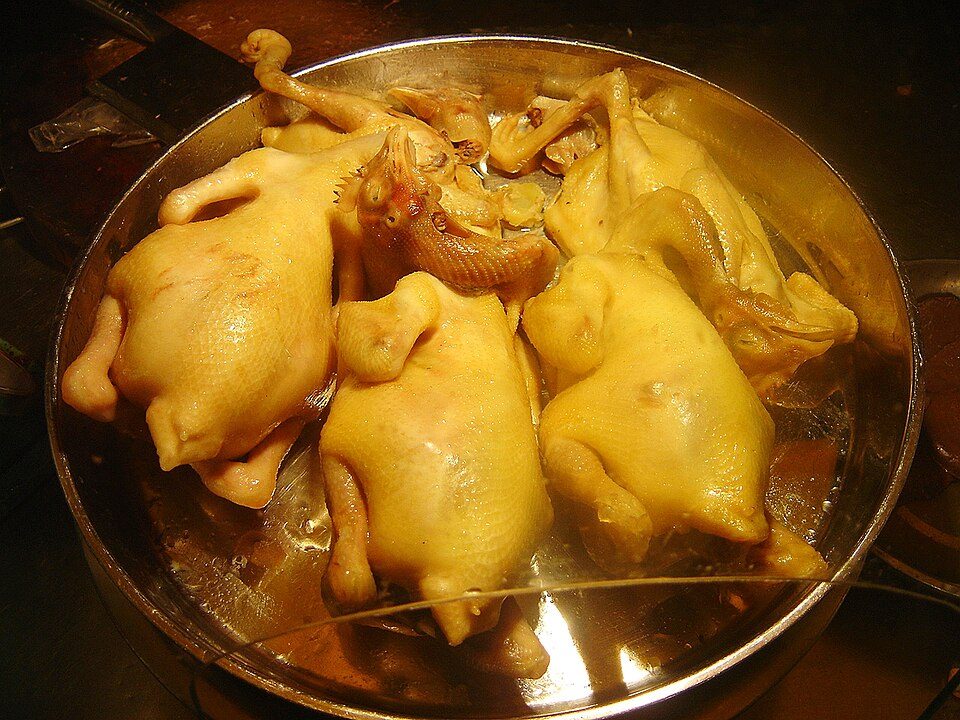Several whole poached yellow-skinned chickens in a steel tray, in Haikou, Hainan
