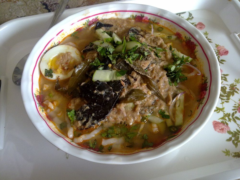 A bowl of Laksa Kedah with a halved boiled egg, cucumber and herbs on a thick fish broth over rice noodles