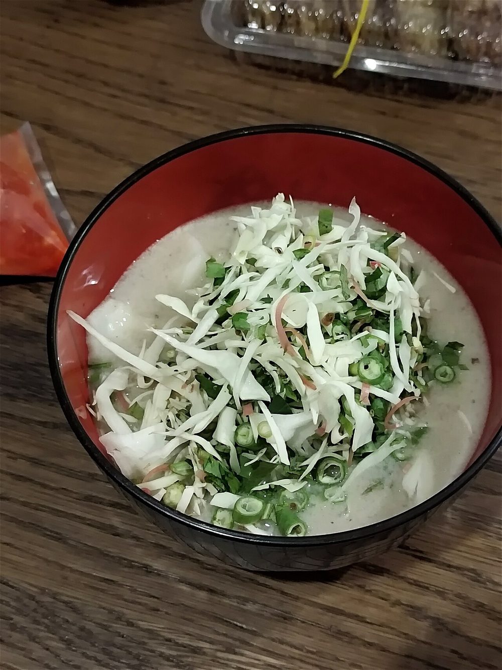 A bowl of laksam: rolled rice noodles under a white coconut and fish gravy, topped with shredded raw cabbage, cucumber and herbs