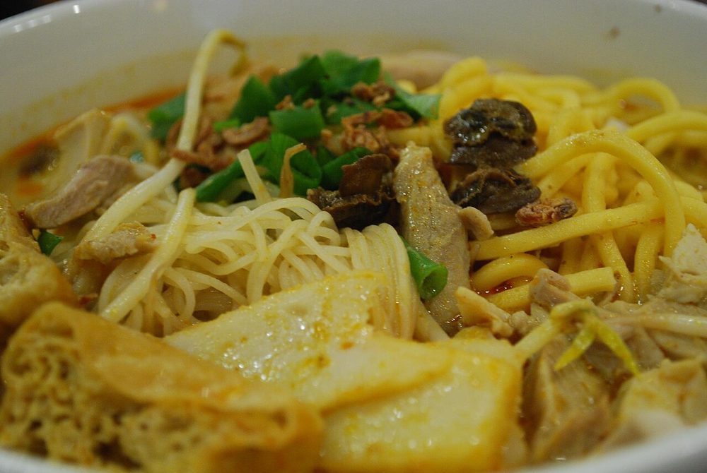 Close-up of a bowl of curry laksa in Melbourne with yellow egg noodles, tau pok, chicken and spring onion in orange gravy
